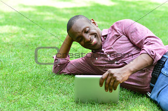 Smiling man lying on the lawn with tablet