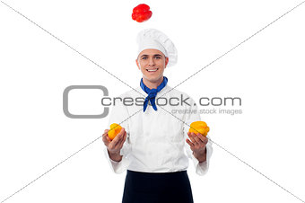 Skilled chef juggling with capsicums