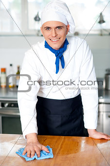 Smiling male chef cleaning the kitchen table