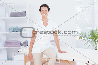 Smiling doctor looking at camera sitting on massage table