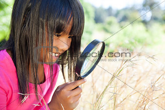 Cute little girl using magnifying glass in park