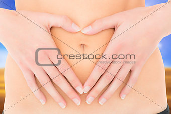 Composite image of mid section of a fit woman with hands over belly