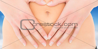 Composite image of mid section of a fit woman with hands over belly