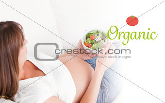 Organic against charming pregnant woman eating a salad while lying on a sofa