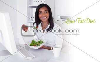 Low fat diet against happy pretty businesswoman eating a salad at her desk