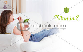 Vitamin e against pretty pregnant woman eating a salad while lying on a sofa