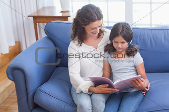 Happy mother and daughter sitting on the couch and reading book