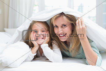Mother and daughter looking at camera under the duvet
