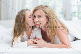 Daughter kissing her mother on the cheek in the bed