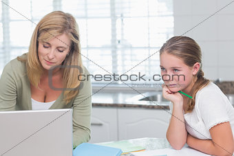 Mother using laptop while daughter doing homework