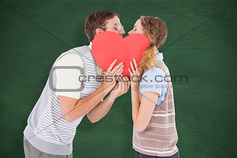 Composite image of geeky hipster couple kissing behind heart card