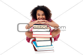 Cute school girl leaning over stack of books