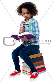 Little girl reading book using magnifying glass