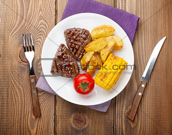 Steak with grilled potato, corn and salad on wooden table