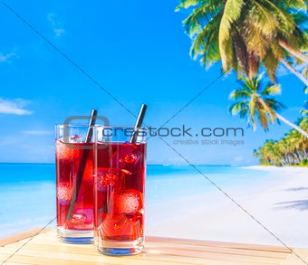 two glasses of red cocktail with blur beach and palm