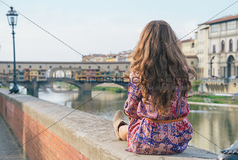 Young woman sitting near ponte vecchio in florence, italy. rear 