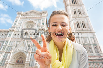 Happy young woman showing victory gesture in front of duomo in f