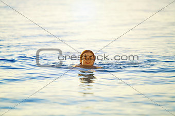 smiling girl swims in the sea at dawn