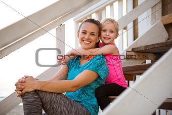 Healthy mother and baby girl hugging on stairs of beach house