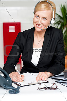 Smiling woman wearing headset writing on notepad