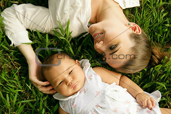 Mother With Caressing Baby Daughter Laying On Grass