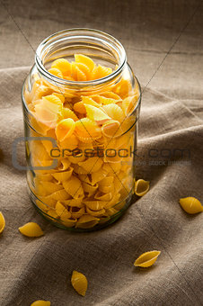 Shell macaroni pasta in glass bowl on hessian fabric cloth background