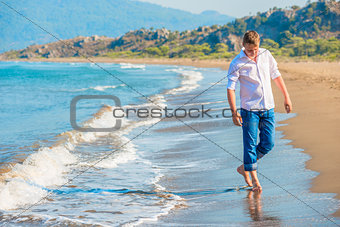 man in jeans and a white shirt walking along the seashore