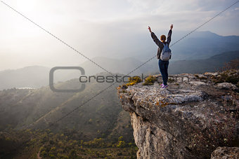 Young woman standing on cliff with outstretched arms and enjoying valley view