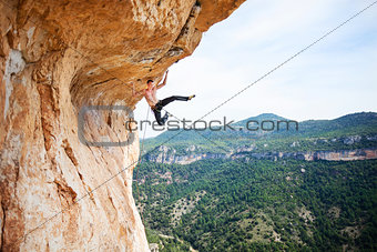 Young man climbing up ledge of cliff, on challenging part of route