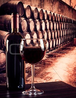 red wine glass near bottle in old wine cellar background