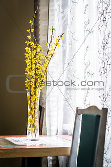 Spring yellow flowers in vase on a table near the window