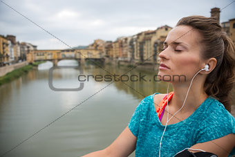 Relaxed fitness woman listening music in front of ponte vecchio 