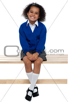 Pretty school girl seated comfortably on a bench