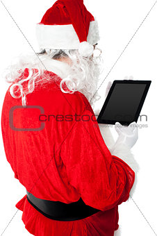 Back view of Santa looking at tablet device screen