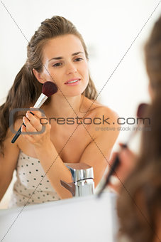 Happy young woman applying makeup in bathroom