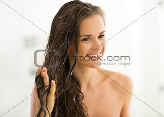 Portrait of happy young woman applying hair mask in bathroom
