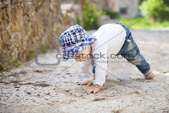 Cute little boy laughing while crawling on stone paved sidewalk