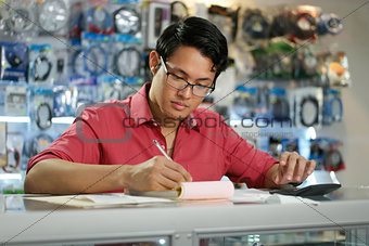 Chinese Man Working In Computer Shop Checking Bills And Taxes
