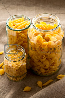 Different types of yellow macaroni pasta in glass bowl on hessian fabric cloth background