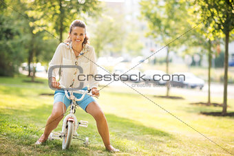 Mother pretending to ride a child's bike in a sunny city park
