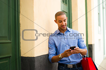 African American Man Shopping And Text Messaging On Phone