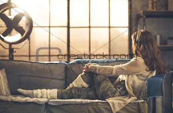 Woman in casual clothing sitting on sofa looking out