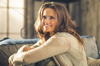 Smiling woman looking up, hugging her knees on sofa