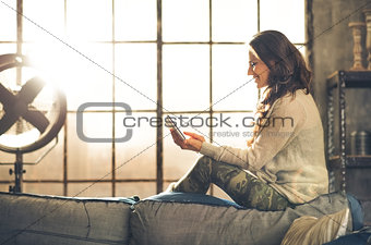 Smiling woman relaxing on back of sofa holding a tablet PC