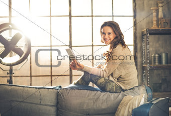 Smiling woman sitting on back of sofa looking up from table pc