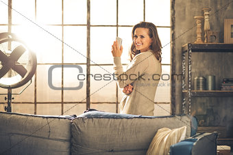 Looking back, a brunette is smiling standing by a loft window