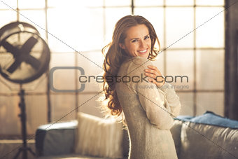 Casual brunette hugging herself while smiling in loft apartment