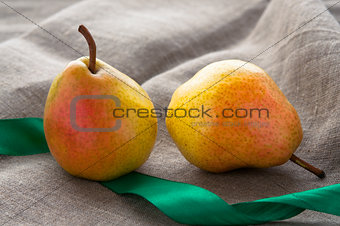 Art still life with small red pears and green ribbonon hessian linen fabric cloth background
