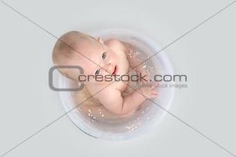 Cute baby having a bath in transparent bucket and playing
