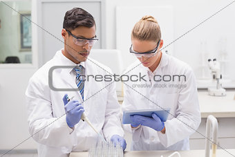 Scientists examining tubes in tray using tablet pc